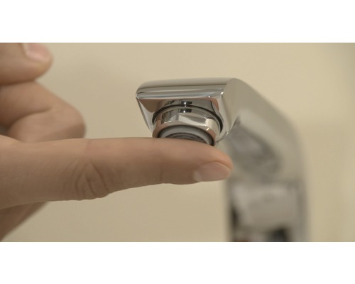 Detailný záber ruky dotýkajúcej sa perlátora vodovodnej batérie