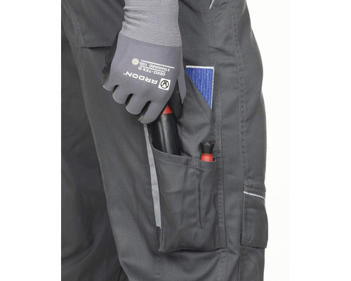 Detailný záber pracovných nohavíc s náradím vo vrecku, nosených s pracovnými rukavicami