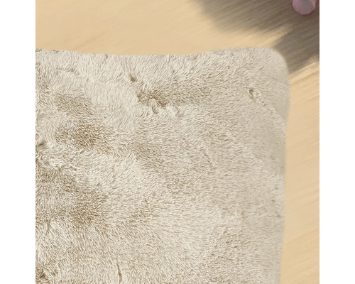 Detail béžového obdĺžnikového koberca s vysokým vlasom.