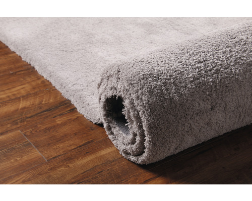 Sivý koberec na drevenej podlahe, čiastočne zrolovaný