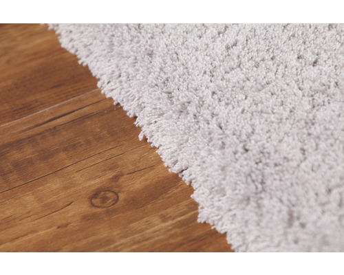 Detailný pohľad na svetlý koberec s vysokým vlasom na drevenej podlahe