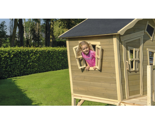 Dieťa sa hrá v drevenom domčeku s oknom na záhrade.