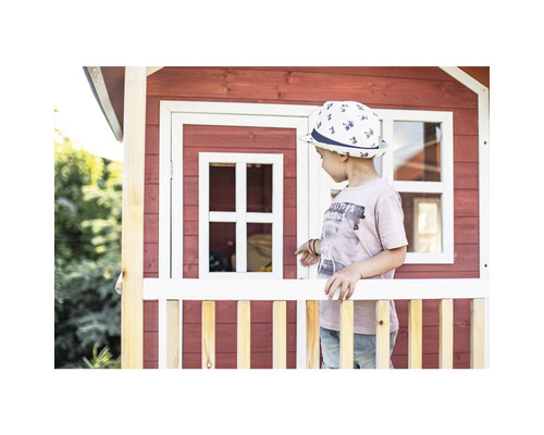 Dieťa stojí pred červeným dreveným hracím domčekom s bielymi prvkami