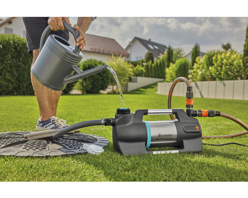 Osoba plní záhradné čerpadlo kanvou na zalievanie v záhrade