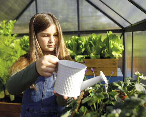 Dievča zalieva rastliny v skleníku kanvou.