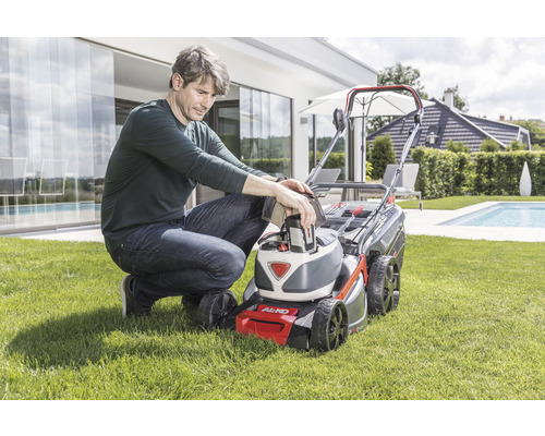 Muž vkladá batériu do kosačky na trávu v záhrade