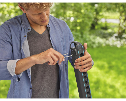 Muž montuje záhradný hadicový vozík pomocou montážneho nástroja v záhrade.