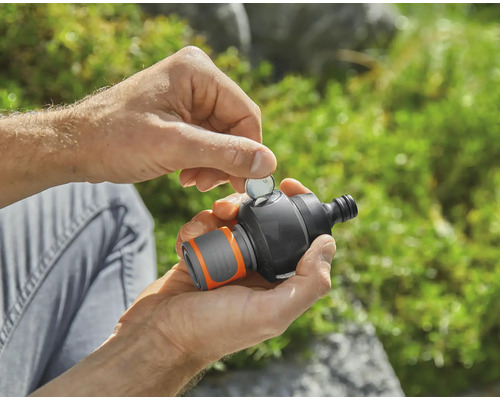 Osoba vkladá mincu do záhradného časovača vody.