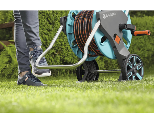 Záhradná scéna s osobou ovládajúcou nohou bubon na hadicu Gardena