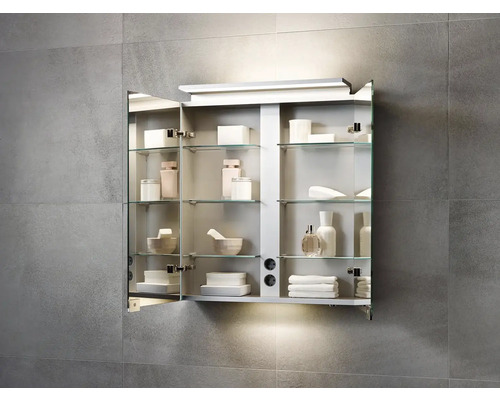 Otvorená zrkadlová skrinka so sklenenými policami a rôznymi kúpeľňovými potrebami na sivej stene