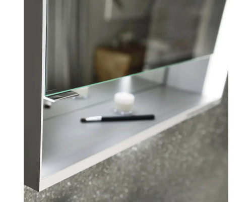 Detailný pohľad na zrkadlovú skrinku s policou, na ktorej je sviečka a štetec