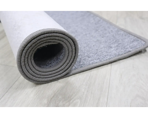 Sivý koberec zrolovaný na svetlej drevenej podlahe