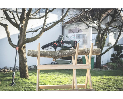 Akumulátorová reťazová píla na drevenom kozlíku s kmeňom stromu v záhrade