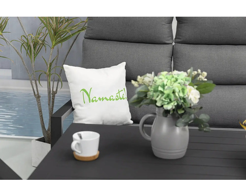 Dekoratívne aranžmán s vankúšom s nápisom Namaste, váza s kvetmi, šálka a rastlina na sedacej súprave