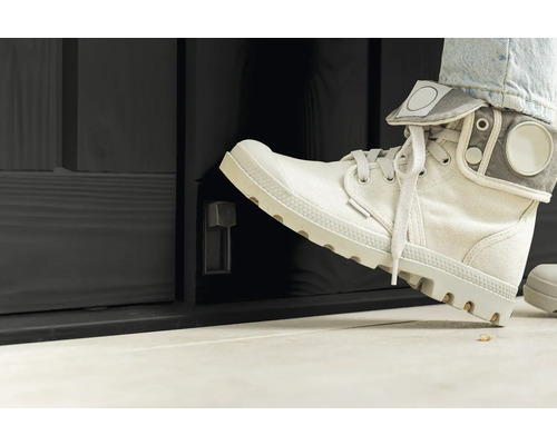 Osoba otvára nohou čierne vonkajšie dvere s otočným gombíkom