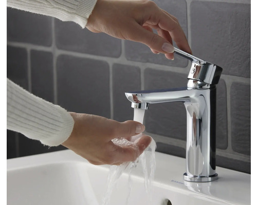 Žena si umýva ruky pod chrómovou umývadlovou batériou.