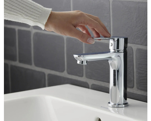 Ruka ovláda chrómovanú umývadlovú batériu na umývadle.