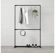 Čierny stojan na šaty s oblečením, klobúkom, topánkami a závesnou rastlinou pred tehlovou stenou.