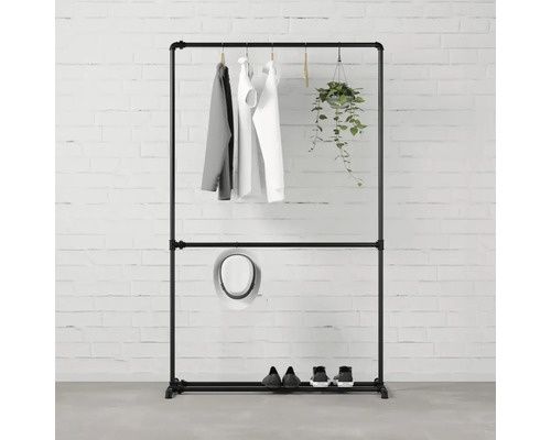 Čierny stojan na šaty s oblečením, klobúkom, topánkami a závesnou rastlinou pred tehlovou stenou.