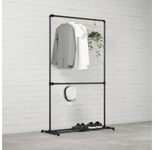 Čierny vešiak na šaty s oblečením, klobúkom, topánkami a rastlinou pred tehlovou stenou