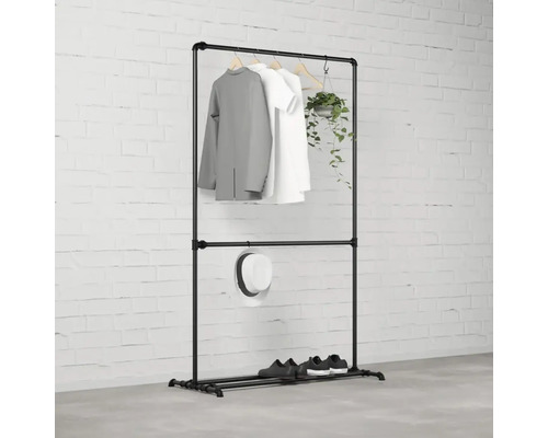 Čierny vešiak na šaty s oblečením, klobúkom, topánkami a rastlinou pred tehlovou stenou