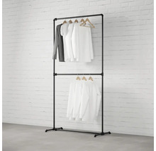 Čierny vešiak na oblečenie s dvomi úrovňami a oblečením na drevených vešiakoch pred tehlovou stenou