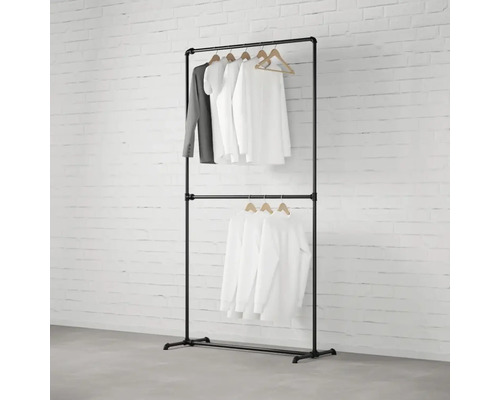 Čierny vešiak na oblečenie s dvomi úrovňami a oblečením na drevených vešiakoch pred tehlovou stenou