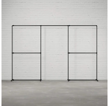 Čierny, modulárny šatník so stojanom na odevy z kovových rúrok na pozadí bielej tehlovej steny.