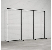 Šatníkový stojan z oceľových rúrok v industriálnom dizajne pred bielou tehlovou stenou.