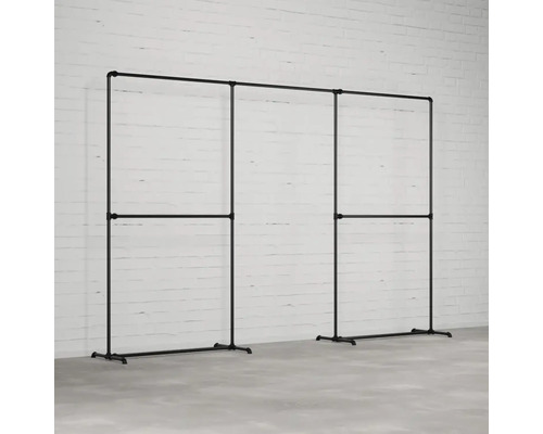 Šatníkový stojan z oceľových rúrok v industriálnom dizajne pred bielou tehlovou stenou.