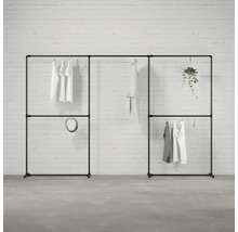 Čierny modulárny šatníkový systém s oblečením a dekoráciou pred tehlovou stenou