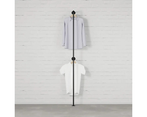Čierny vešiak na oblečenie s dvoma kusmi oblečenia pred tehlovou stenou