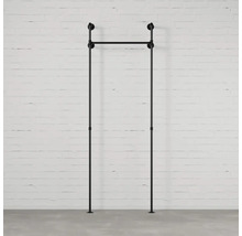 Čierny vešiak na oblečenie z kovových rúrok pred bielou tehlovou stenou