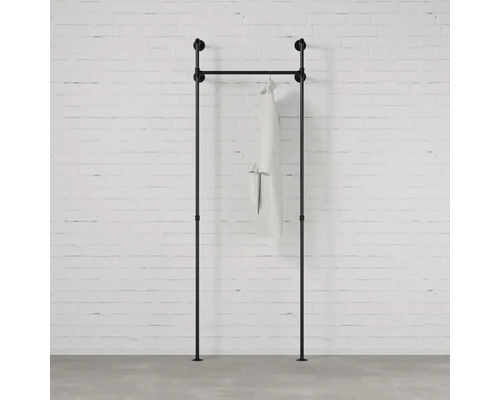 Čierna šatníková tyč z rúrok s odevom pred tehlovou stenou