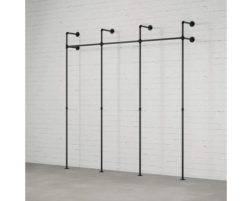 Čierny kovový vešiak na oblečenie z rúrok pred bielou tehlovou stenou