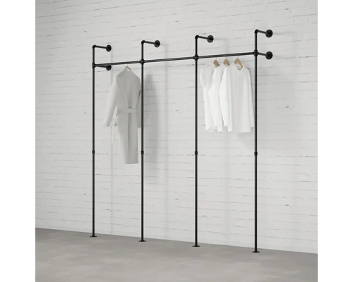 Čierny rúrkový systém na šaty so zaveseným oblečením pred tehlovou stenou