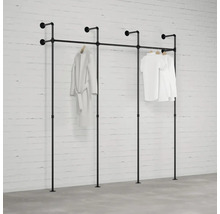 Čierna kombinácia šatníkového stojana z rúrok pred bielou tehlovou stenou so zaveseným oblečením.