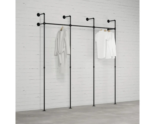 Čierna kombinácia šatníkového stojana z rúrok pred bielou tehlovou stenou so zaveseným oblečením.