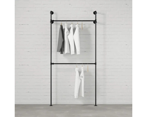 Stojan na oblečenie z rúrok so zaveseným oblečením pred tehlovou stenou