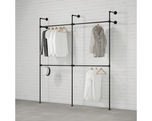 Vešiak na šaty z rúrok so zaveseným oblečením pred tehlovou stenou