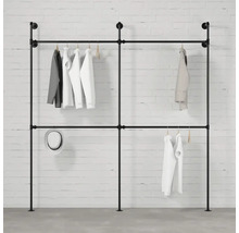 Voľne stojaca šatníková tyč z rúrok so zaveseným oblečením na pozadí bielej tehlovej steny.