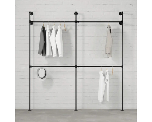 Voľne stojaca šatníková tyč z rúrok so zaveseným oblečením na pozadí bielej tehlovej steny.