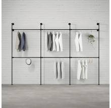 Čierny kovový rúrkový vešiak na šaty s oblečením pred tehlovou stenou