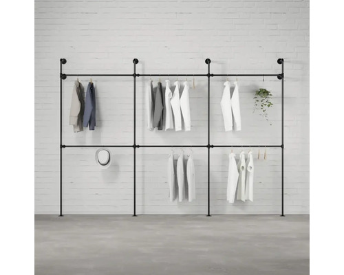 Čierny kovový rúrkový vešiak na šaty s oblečením pred tehlovou stenou