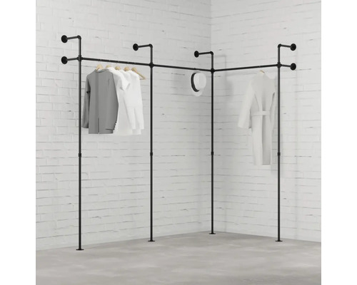 Rohový vešiak na šaty z rúrok s oblečením pred tehlovou stenou