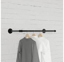 Nástenná šatníková tyč z kovovej rúrky s oblečením na drevených vešiakoch pred tehlovou stenou