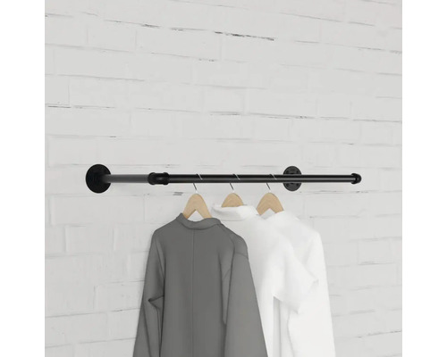 Nástenná šatníková tyč z kovovej rúrky s oblečením na drevených vešiakoch pred tehlovou stenou