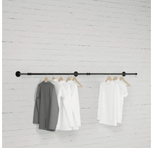 Čierna šatníková tyč so zaveseným oblečením pred tehlovou stenou