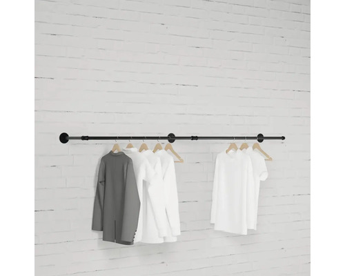 Čierna šatníková tyč so zaveseným oblečením pred tehlovou stenou