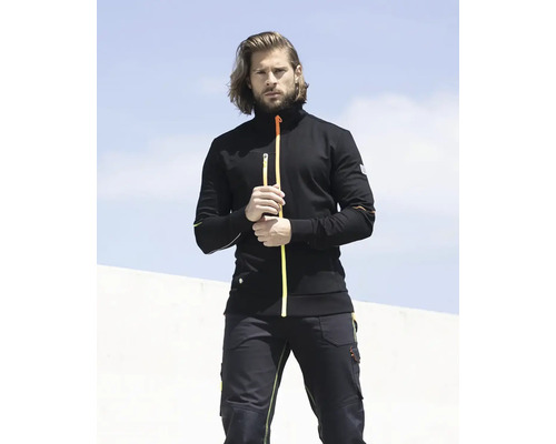 Muž má na sebe pracovnú bundu a pracovné nohavice.